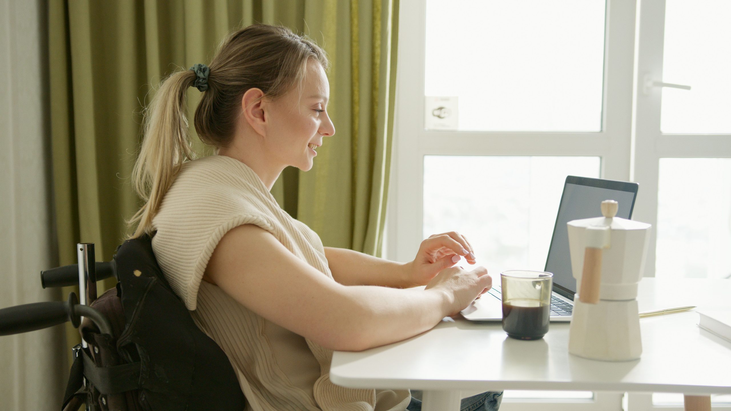 Femme en fauteuil roulant avec café travaillant sur laptop